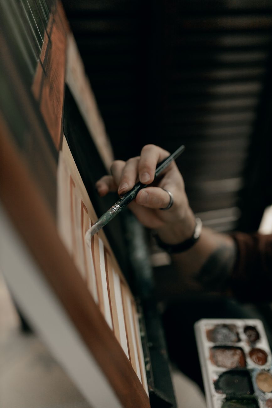 Artist's hand painting canvas in studio with brush and palette.